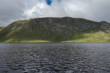 A serene view of Lough Veagh, in Ireland, showcasing tranquil waters, lush greenery, and misty...