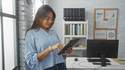 Young woman using tablet in modern office workplace indoors with bookshelf and computer in background