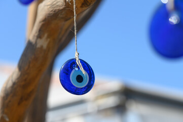 Bright blue glass talisman catches sunlight while hanging from a twisted branch against a clear sky