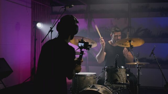 Shooting a music video. The director of photography makes a video, shoots a drummer musician. The view behind the scenes. Create a music video for a rock band. Creative director and crew.