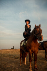Fototapeta premium elegant girl in long dress, gloves and hat upside down on horse, in the middle of field.