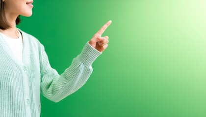 新緑のグラデーション背景に伸びる淡いブルーのカーディガンを着た手、春風を感じる指し示しの瞬間。

