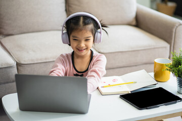 Adorable attentive Little girl writing in notebook and using laptop while doing homework.