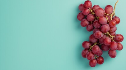 Flat lay of a bunch of red grapes on a light blue background. the grapes are clustered together in a bunch, with some of them overlapping each other.