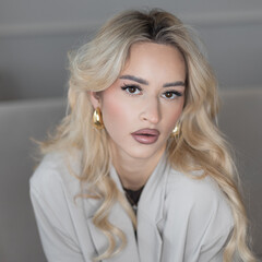 Glamorous beautiful stylish blonde woman in fashionable clothes with blazer sitting on sofa and...