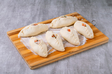 Raw rasstegai made from yeast dough with fish filling on a wooden board with flour. Preparation for baking, proofing of pies. Step by step