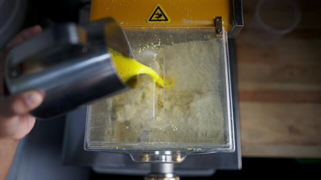 Close up view in slow motion of a Chef adding liquid ingredients to a pasta dough maker machine in a restaurant,