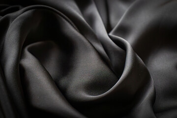 Fototapeta premium Elegant black silk flows smoothly to create soft waves and deep folds. The smooth texture reflects the light, highlighting the luxury and sophistication of the material. Perfect for backdrops, fashion