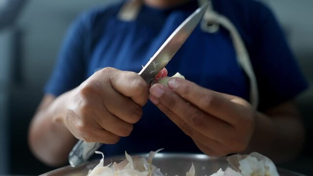 Close up cinematic view of two hands peeling garlic with a knife in a restaurant kitchen.