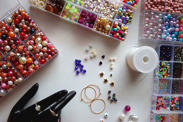 Hand figurine, colorful friendship bracelets, necklaces, various beads and DIY supplies on the table. Making jewelry at home. Flat lay.