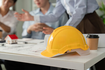 Construction Meeting and Safety Protocols. A hard hat rests on the table during a design discussion among building professionals.