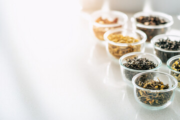 Assorted dried tea herbs, neatly arranged in small glass containers on a smooth white countertop