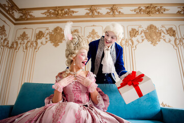 Elegant aristocratic couple exchanging a gift in a vintage baroque interior with joyful expressions