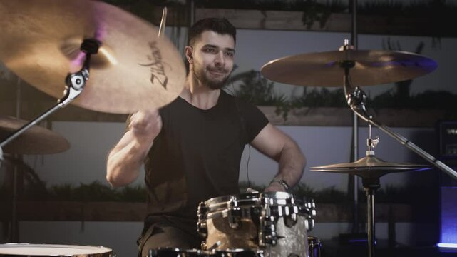 A young attractive male drummer plays with sticks on a drum kit. Makes hits on metal cymbals or Crash. Home rehearsal studio for recording sound and songs. Plays rock or heavy metal music.
