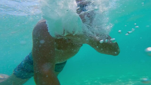 Underwater view of a swimmer under shark attack in a turquoise sea making bubbles, slow motion