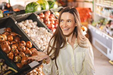 Happy woman standing near stall vegetables on the farmer market and point hand at side. Girl look happy and smiling. 