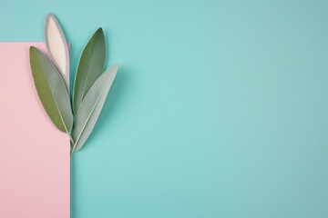 Obraz premium Delightful pastel paper layers with playful bunny ears and fresh sage leaves create a serene Easter vibe