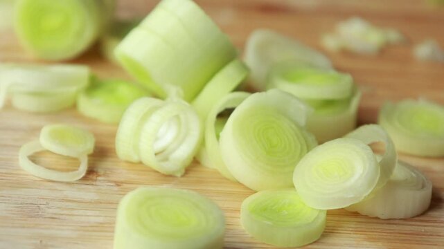 woman's hands carefully slicing fresh leek on a wooden cutting board