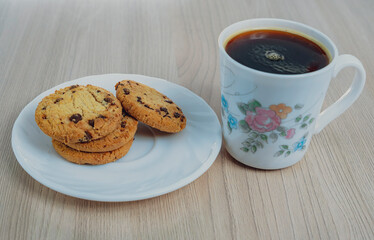 Coffee in floral mug with chocolate chip cookies on wooden table