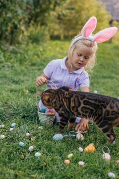 Young girl with bunny ears playing with Easter eggs and a cat