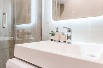Modern bathroom detail featuring a white sink, chrome faucet, and sleek accessories. The lighting is bright and highlights the clean design.