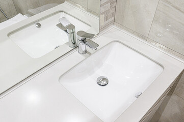 modern bathroom sink with a chrome faucet and clean white countertop. Reflected in the mirror above