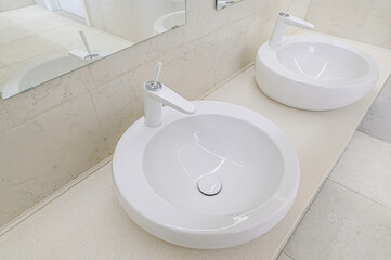 Bright bathroom featuring two modern, round white sinks, white faucets, light tile walls and mirrors.