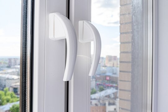 Close-up of a white window with two handles, showing a cityscape view through the glass. - Powered by Adobe