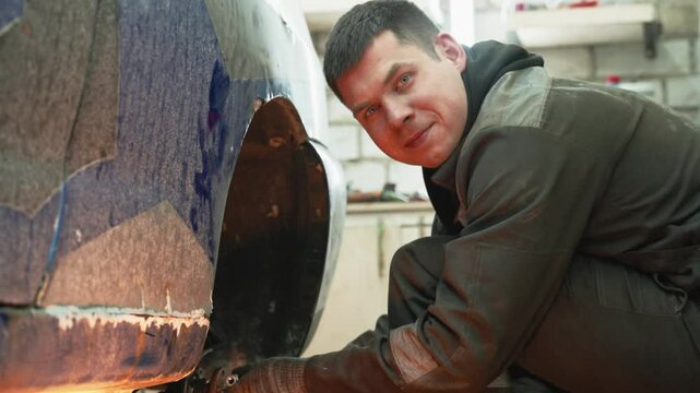 Skilled automotive technician repairing damaged wheel arch, carefully grinding metal surface and applying professional restoration techniques inside modern workshop