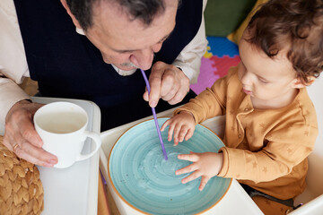A grandfather and his grandson are enjoying time together, playing with water and straws while sitting at a colorful table with drinks