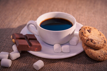 Top view of coffee with chocolate, cookie, and marshmallows on burlap