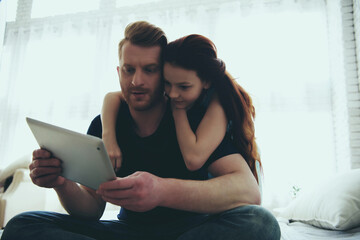 Red haired father and teen daughter are looking at computer tablet. Child education concept. Family...