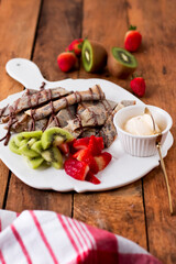 Nutella Crepes with sliced kiwi, strawberries, and a scoop of ice cream served on a white plate isolated wooden table side view delicious sweet treat
