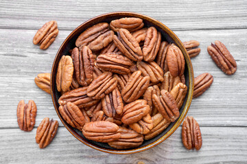 Photograph of dried pecan nuts without shell in a bowl on wooden background. Top view. Healthy eating and snack, whole foods. Natural fats, fibre, minerals, vitamins.