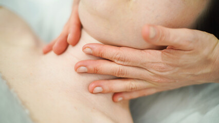 A woman lies on a massage table and the masseur's hands massage her neck. closeup.  soft focus.