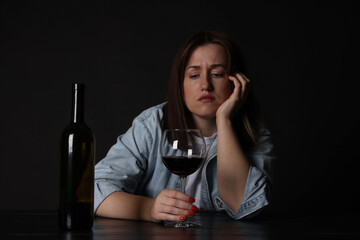 Alcohol addiction. Miserable woman with wine at table in dark