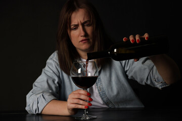 Alcohol addiction. Miserable woman pouring wine into glass at table in dark
