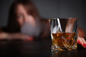 Alcohol addiction. Woman with glass of whiskey at wooden table indoors, selective focus