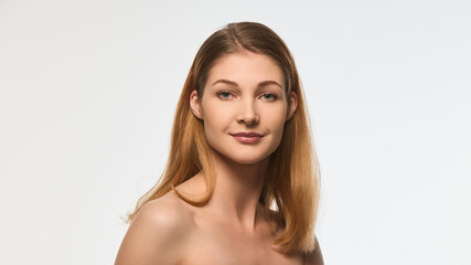 Fototapeta premium Charming woman with radiant skin and delicate smile, natural makeup, smooth hair cascading over shoulder, looking into camera. Concept of beauty, skincare, wellness, self-care, cosmetics, femininity.