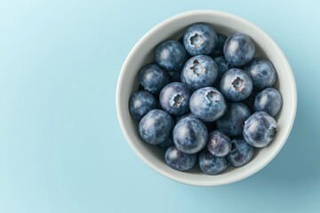 Fresh blueberries arranged in white bowl on soft blue background