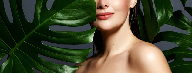 A woman partially hidden behind a large tropical leaf highlights natural beauty and a fresh, eco-friendly skincare concept. Living green