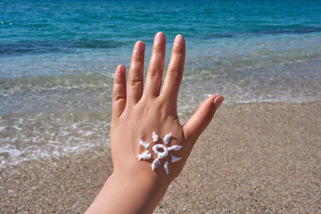Female  hand with a sun shape symbol drawn in sunscreen lotion on a beach, highlighting summer...