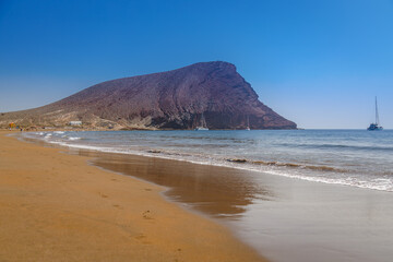 Montana Roja, a volcanic cone in Tenerife, rises above a serene beach with gentle waves