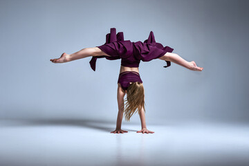 Young female dancer in purple dress performing an acrobatic handstand