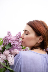 Naklejka premium A young woman with a bouquet of lilacs in her hands inhales the fragrance of flowers against the background of nature.