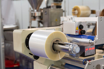 A roll of plastic film above a packaging conveyor for food packaging or plastic packaging bag...