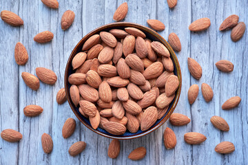 Photograph of dried almonds nuts in a bowl on wooden background. Top view.  Healthy eating and snack, whole foods. Source of protein and magnesium.