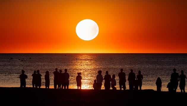 Silhouette of a group of people gathered on a beach at sunset, watching a partial solar eclipse, dramatic sky, cinematic coastal scene