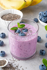Smoothie with blueberries, banana, chia seeds and yogurt in a glass on a gray concrete background. Healthy food.