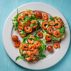 Toast with shrimp, arugula and avocado on a white plate with cherry tomatoes on a blue table. Space for text. Healthy and tasty breakfast concept. Top view. Flat lay.